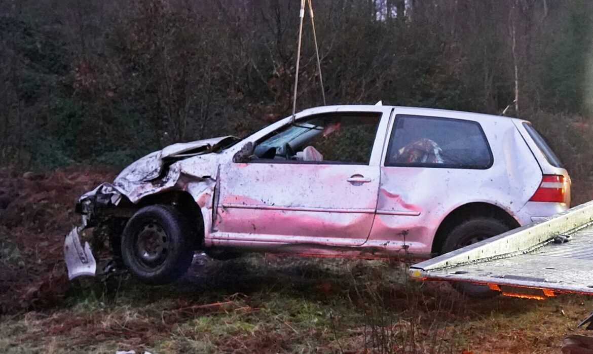 Weißes Auto mit starkem Frontschaden, angehoben von einem Abschleppfahrzeug in ländlicher Umgebung.