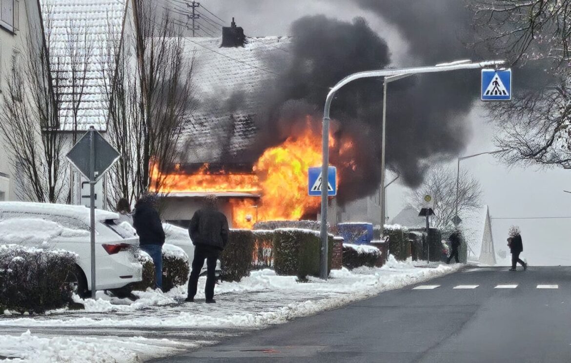 Brennendes Haus in verschneiter Straße mit Rauch und Flammen.