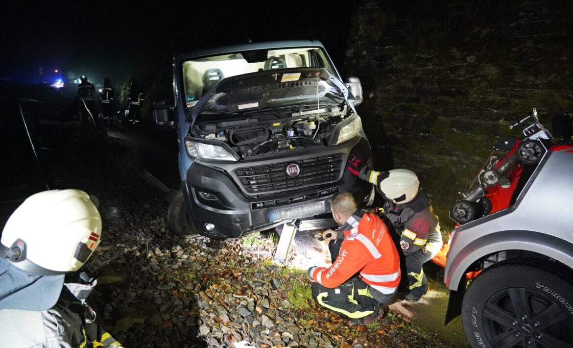 Feuerwehrleute untersuchen einen Lieferwagen im Dunkeln mit geöffneter Motorhaube auf einer Straße.
