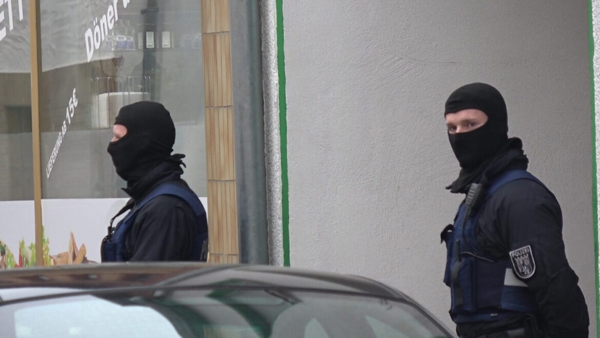 Zwei maskierte Polizisten in Uniform vor einem Geschäft mit Dönerwerbung.