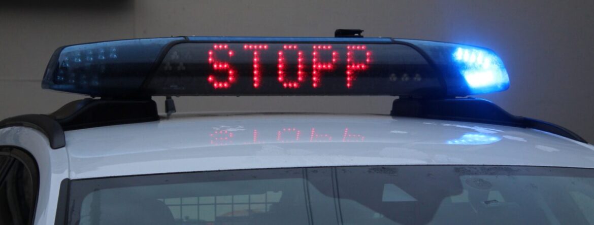 Polizeiauto mit Leuchtschrift "STOPP" und blauem Sirenensignal auf dem Dach.