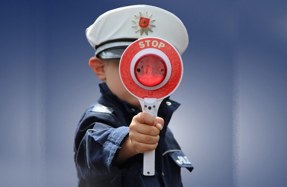 Kind in Polizeiuniform hält ein Stoppsignal hoch, unscharfer blauer Hintergrund.