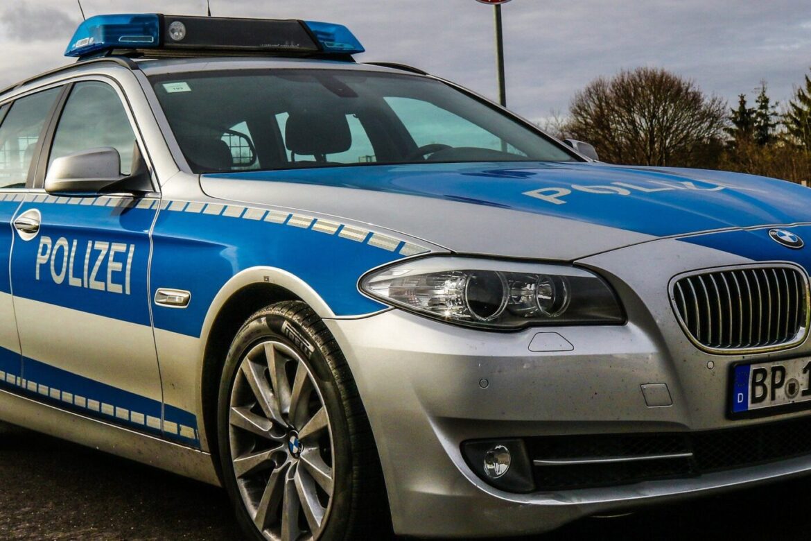 Silbernes und blaues Polizeiauto mit eingeschaltetem Dachlicht auf einer Straße im Freien.