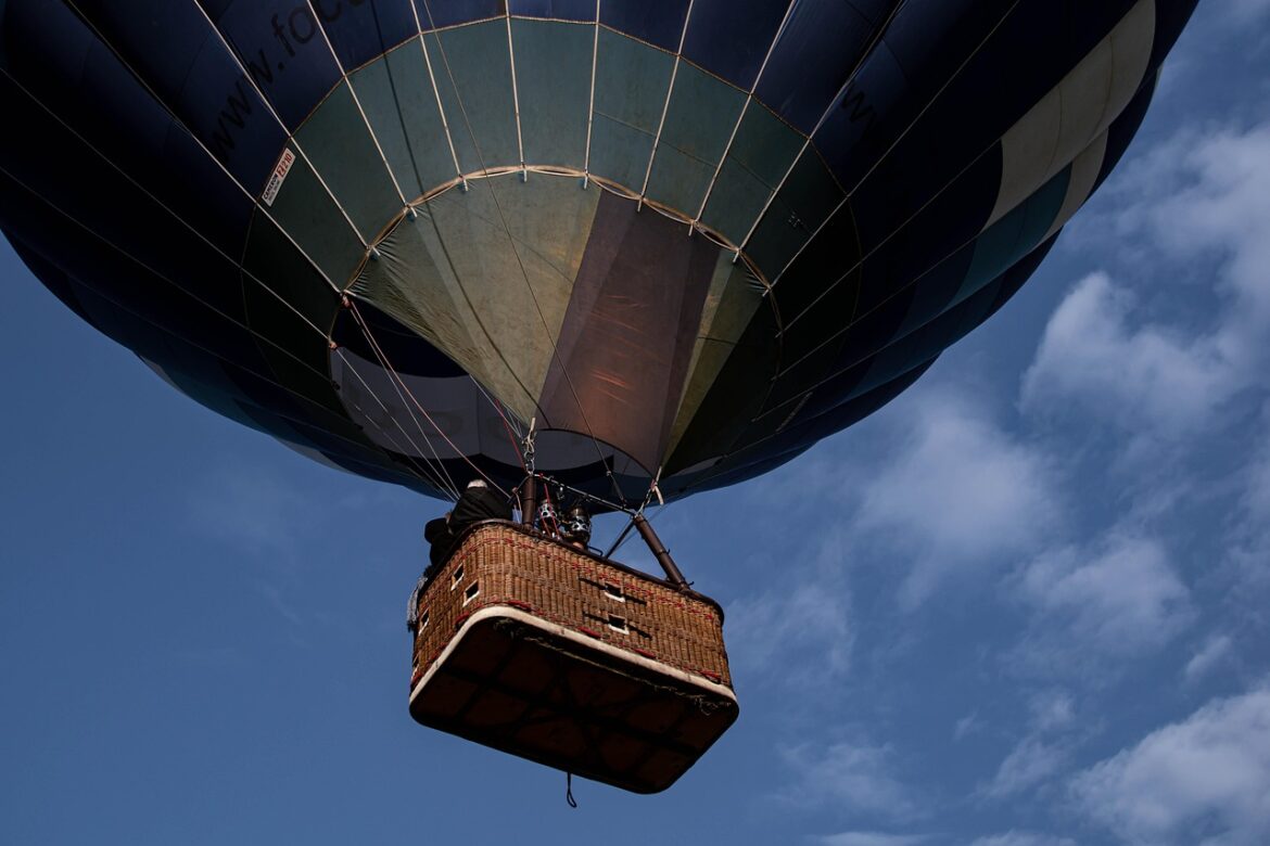 Heißluftballon mit Korb fliegt am Himmel, teilweise bedeckt von Wolken.