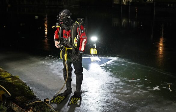56aktuell_yg6cCgSz Taucher in Ausrüstung steht am Ufer eines dunklen Gewässers bei Nacht.