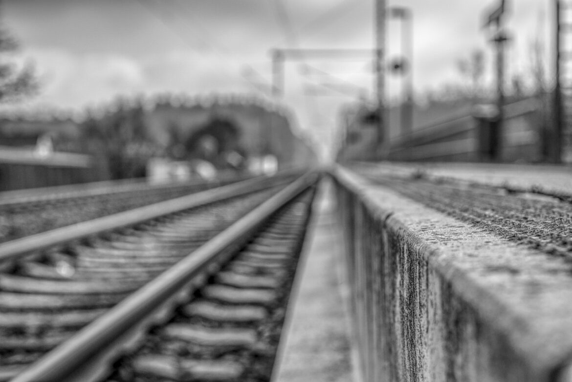 Verschwommene Schwarz-Weiß-Aufnahme von Bahngleisen mit einer Oberleitung.
