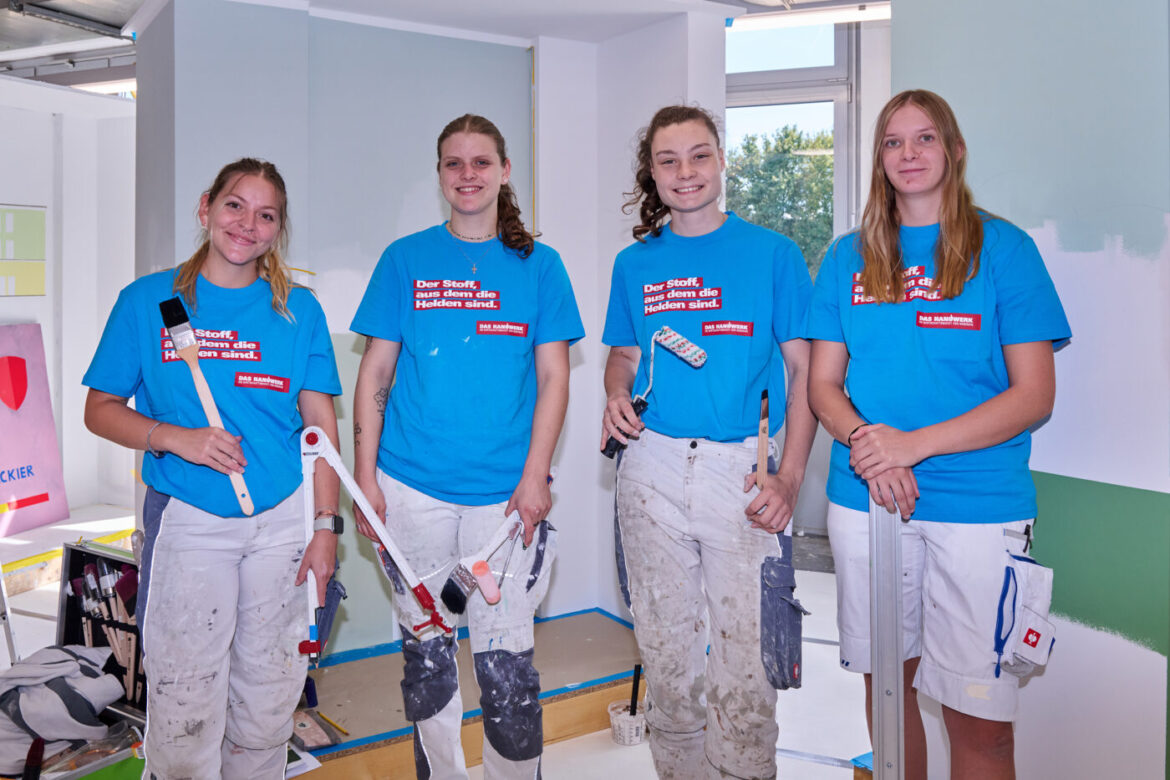 Vier junge Frauen in blauen T-Shirts mit Malerwerkzeugen.