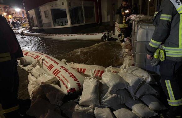 nassau-min_56aktuell Feuerwehrleute sichern eine überflutete Straße mit Sandsäcken.