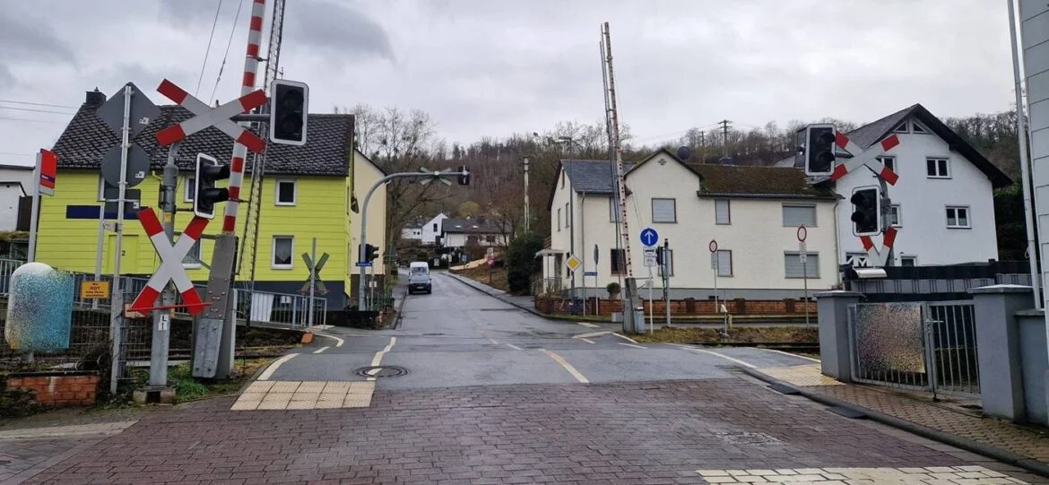 Bahnübergang in Nievern mit Schranken und Häusern im Hintergrund.