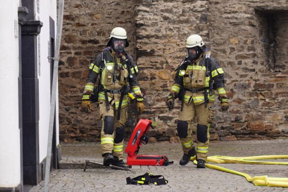 salhofplatz-5-min_56aktuell Zwei Feuerwehrleute in Schutzkleidung vor einer Steinmauer.